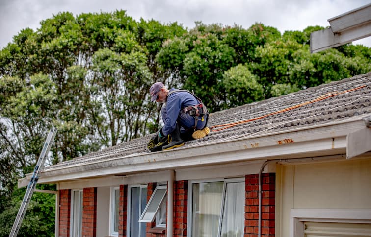Person on roof with harness clearing a blocked gutter